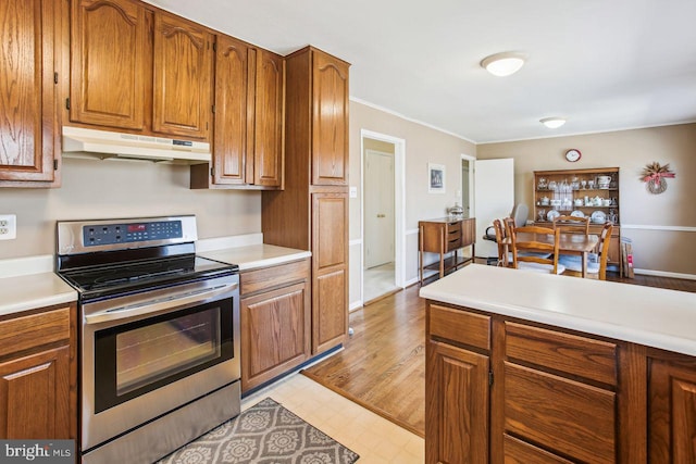 kitchen featuring under cabinet range hood, electric range, brown cabinets, and light countertops