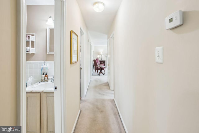 hallway with a sink, baseboards, and light carpet