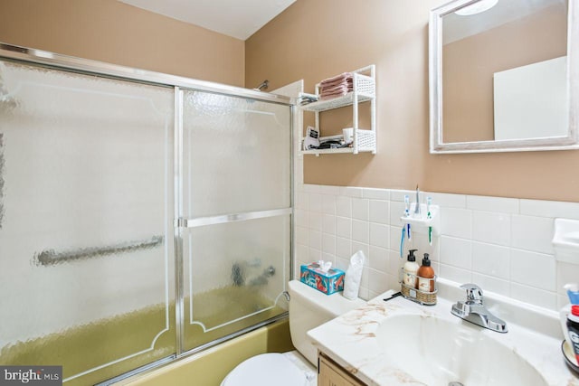 full bathroom featuring shower / bath combination with glass door, tile walls, vanity, and toilet