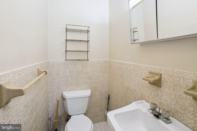 bathroom featuring a sink, toilet, tile walls, and wainscoting