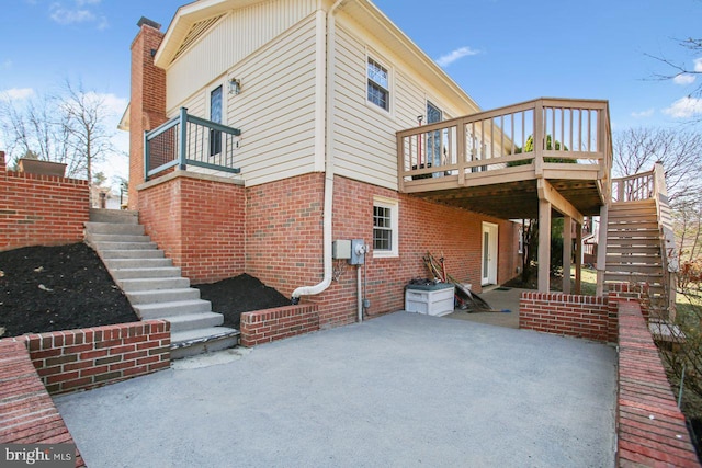 back of property with brick siding, stairway, a chimney, a deck, and a patio