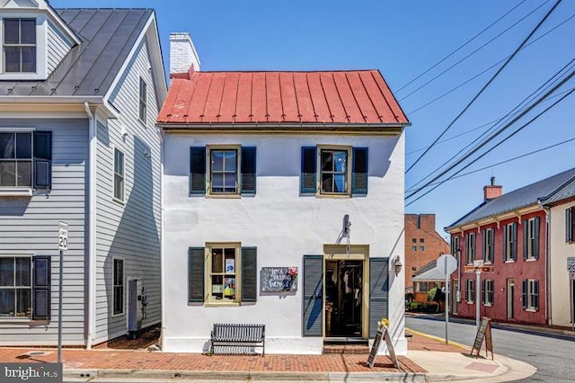 view of front of property featuring a chimney, stucco siding, metal roof, and a standing seam roof