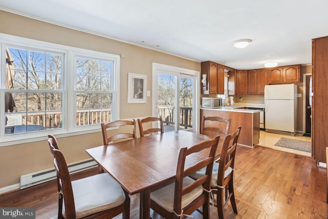 dining area featuring light wood-style flooring, crown molding, a baseboard heating unit, and baseboards