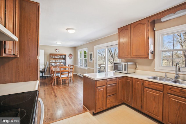 kitchen featuring a sink, stainless steel microwave, a peninsula, and brown cabinetry