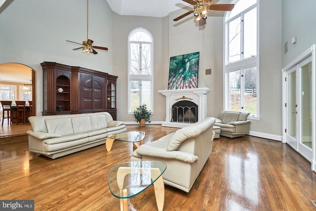 living room with arched walkways, a fireplace with raised hearth, a ceiling fan, and wood finished floors