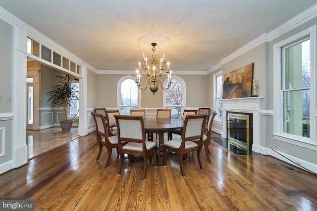 dining room featuring wood finished floors, visible vents, a high end fireplace, crown molding, and a decorative wall