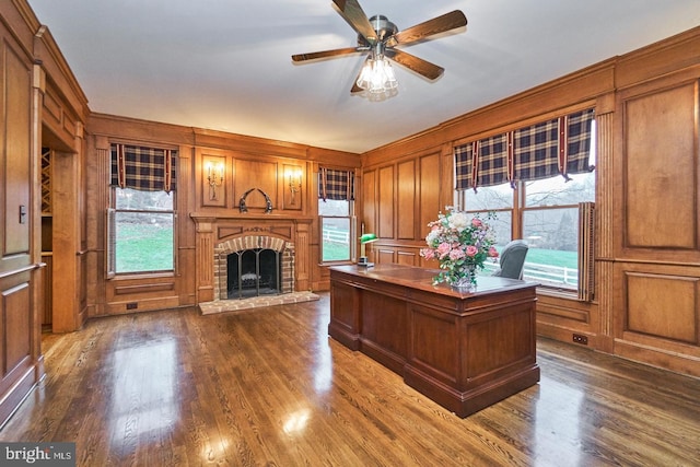 unfurnished office featuring dark wood-type flooring, a decorative wall, a fireplace, and ceiling fan