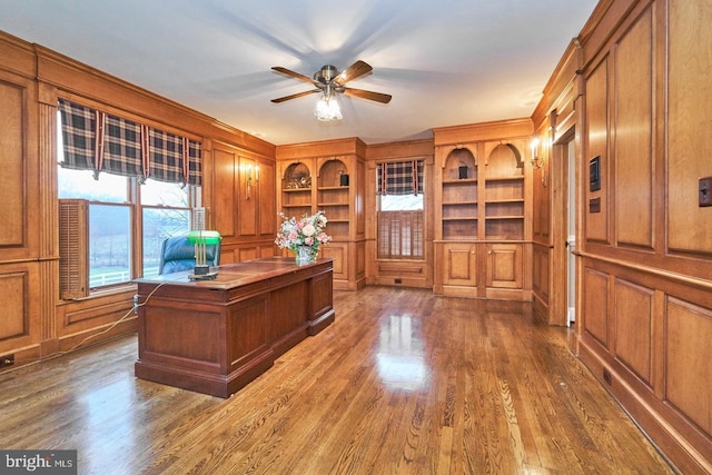 home office with dark wood-style floors, a decorative wall, and a ceiling fan