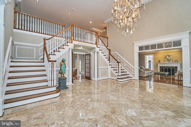 foyer entrance with marble finish floor, ornamental molding, a high ceiling, a decorative wall, and stairs