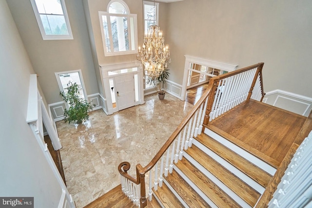 entryway featuring an inviting chandelier, a decorative wall, marble finish floor, and a towering ceiling