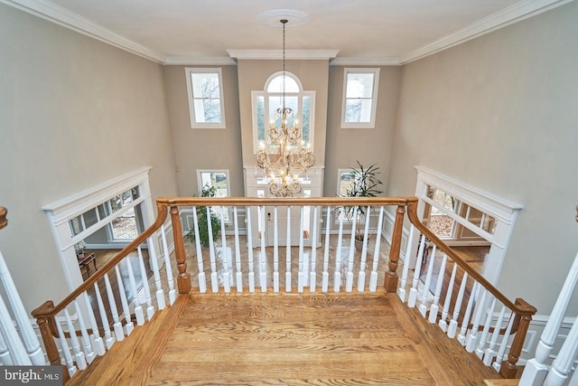 stairs with a healthy amount of sunlight, crown molding, and an inviting chandelier