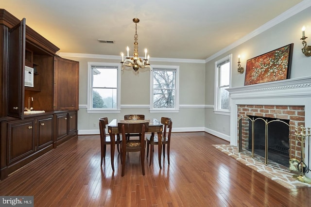 dining area featuring baseboards, visible vents, dark wood finished floors, a fireplace, and ornamental molding