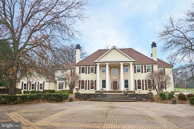 neoclassical home featuring stucco siding and a chimney