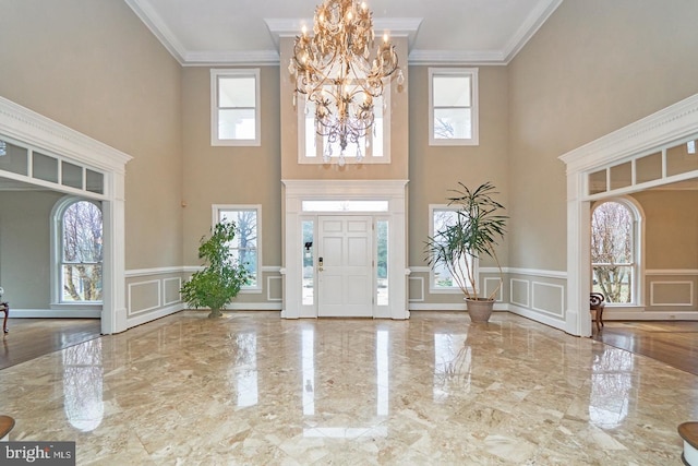 entryway with a decorative wall, marble finish floor, and ornamental molding