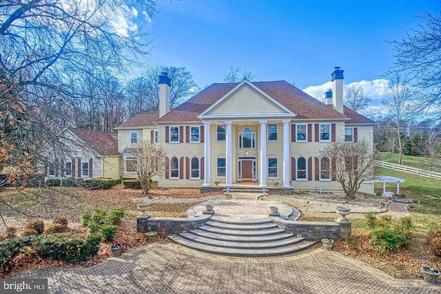 greek revival inspired property featuring stucco siding, fence, and a chimney