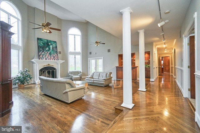 living area featuring ceiling fan, a fireplace, ornate columns, and wood finished floors