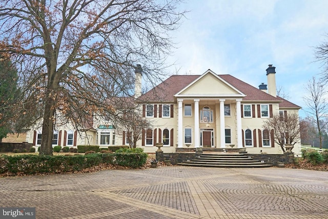 greek revival house featuring stucco siding and a chimney