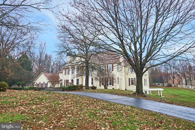 view of front of home with aphalt driveway, stucco siding, a front yard, and fence