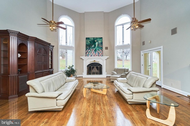 living area featuring a fireplace with raised hearth, baseboards, a ceiling fan, and wood finished floors