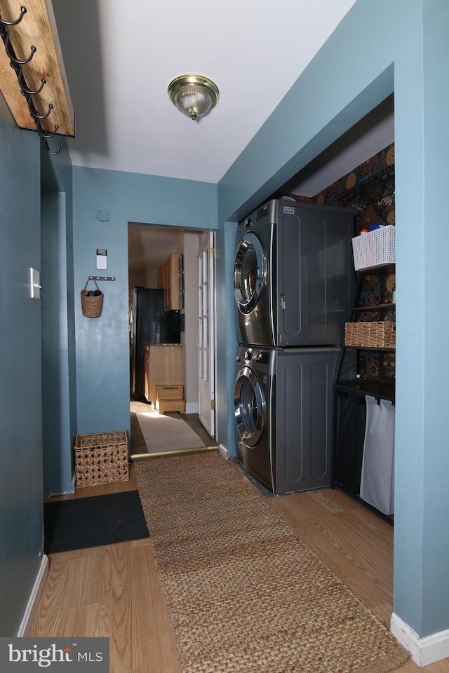 laundry area with wood finished floors, stacked washer and clothes dryer, baseboards, and laundry area