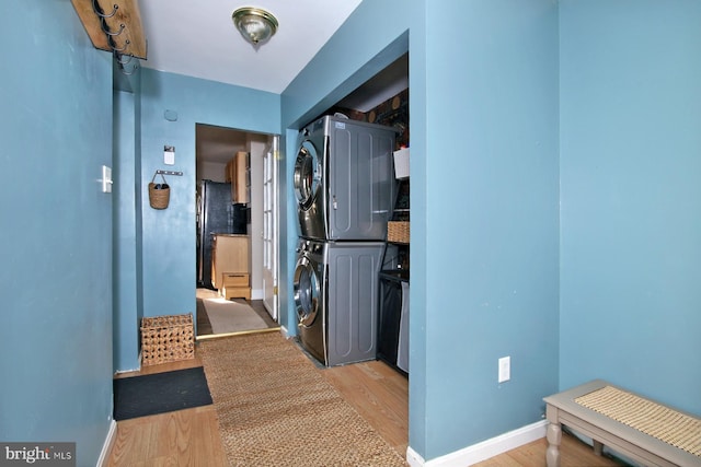 hallway featuring light wood-type flooring, stacked washing maching and dryer, and baseboards