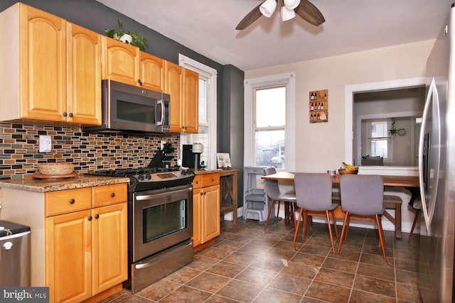 kitchen featuring stainless steel appliances, stone counters, ceiling fan, and backsplash