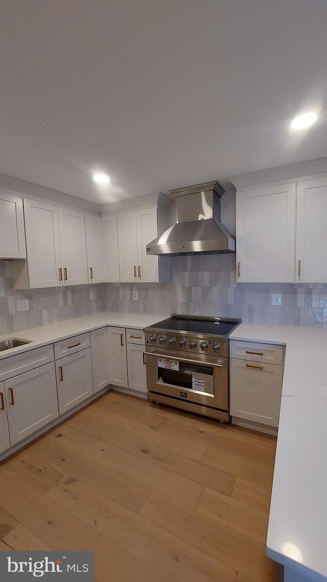 kitchen featuring wall chimney exhaust hood, light countertops, high end range, and white cabinetry