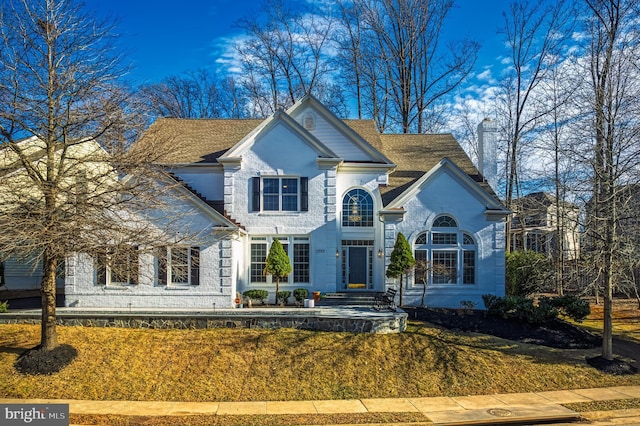 view of front of property with a shingled roof, brick siding, and a chimney