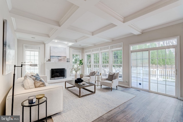 living area with a fireplace with raised hearth, beamed ceiling, coffered ceiling, and wood finished floors