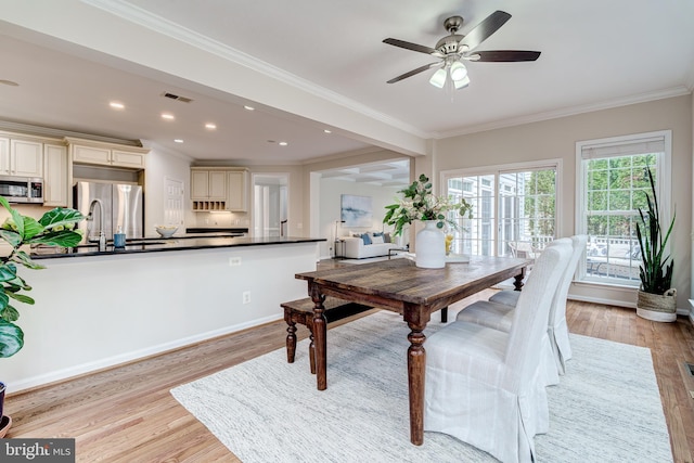 dining room with ceiling fan, light wood finished floors, baseboards, and crown molding