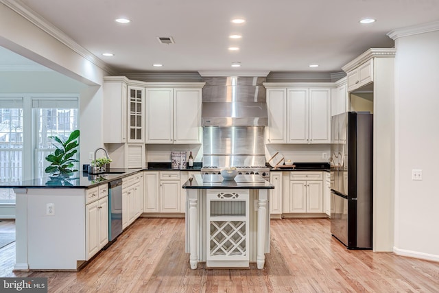 kitchen featuring a sink, visible vents, wall chimney range hood, appliances with stainless steel finishes, and crown molding