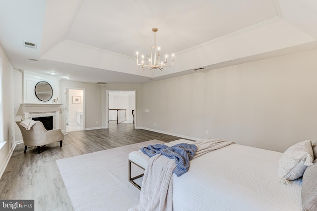 bedroom with light wood-type flooring, a tray ceiling, visible vents, and a premium fireplace