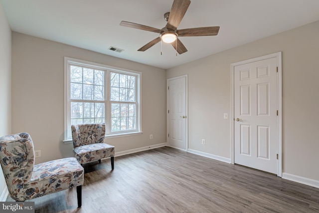 living area featuring baseboards, visible vents, ceiling fan, and wood finished floors