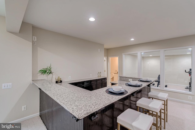 kitchen with recessed lighting, light carpet, baseboards, light stone countertops, and a kitchen bar