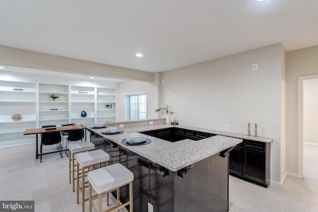 kitchen with light stone counters, a breakfast bar area, recessed lighting, light carpet, and baseboards