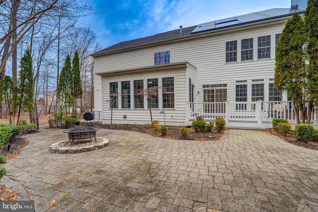 rear view of property with a fire pit, a patio area, and roof mounted solar panels