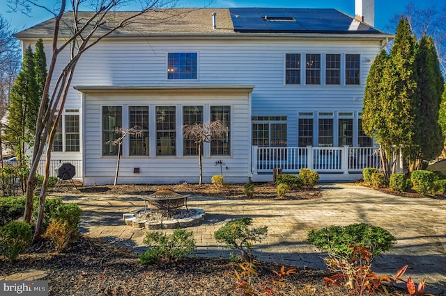 rear view of property featuring a chimney, roof mounted solar panels, a fire pit, and a wooden deck