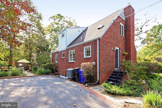 exterior space with brick siding, a chimney, a patio area, fence, and cooling unit