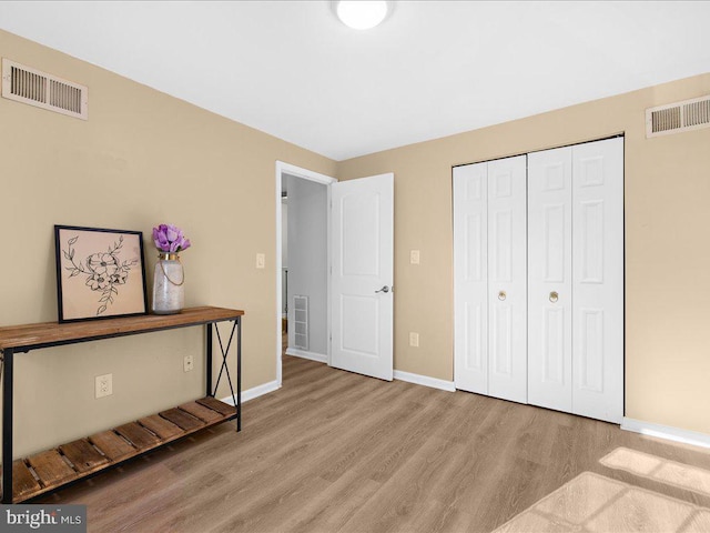 unfurnished bedroom featuring light wood-style flooring, a closet, visible vents, and baseboards