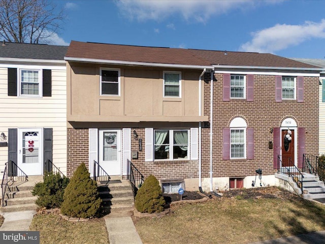 view of property with entry steps, stucco siding, a front lawn, and brick siding