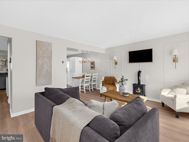 living area featuring a wood stove, light wood-style floors, baseboards, and an inviting chandelier