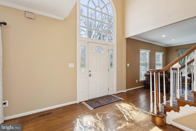 entryway featuring visible vents, crown molding, baseboards, stairway, and wood finished floors