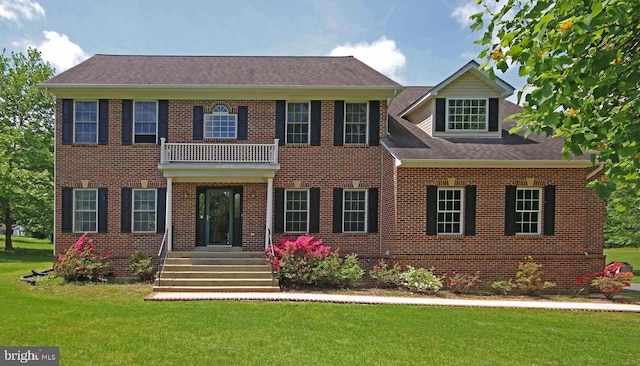 colonial home with brick siding, a balcony, and a front lawn