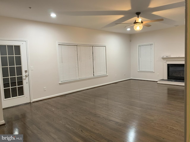 unfurnished living room featuring dark wood-style flooring, recessed lighting, a glass covered fireplace, ceiling fan, and baseboards