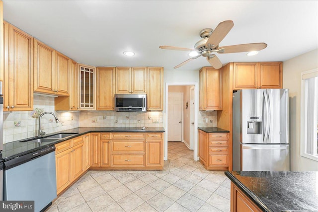 kitchen featuring tasteful backsplash, appliances with stainless steel finishes, glass insert cabinets, a sink, and dark stone countertops