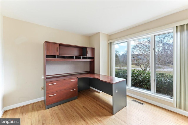 unfurnished office with baseboards, light wood-style flooring, visible vents, and built in desk