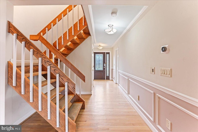 entryway with light wood finished floors, a decorative wall, crown molding, and a wainscoted wall