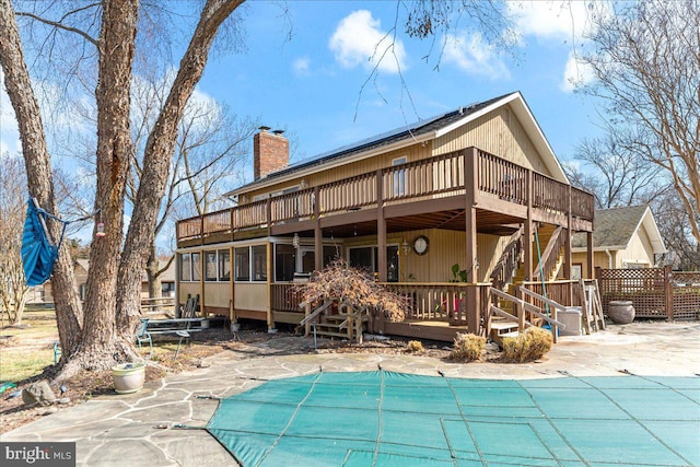 back of property with a covered pool, a chimney, a patio, and a wooden deck