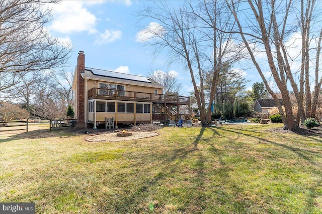 back of property featuring a yard, a chimney, solar panels, a deck, and stairs