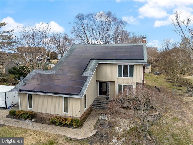 view of front of property featuring solar panels, a shingled roof, and a chimney